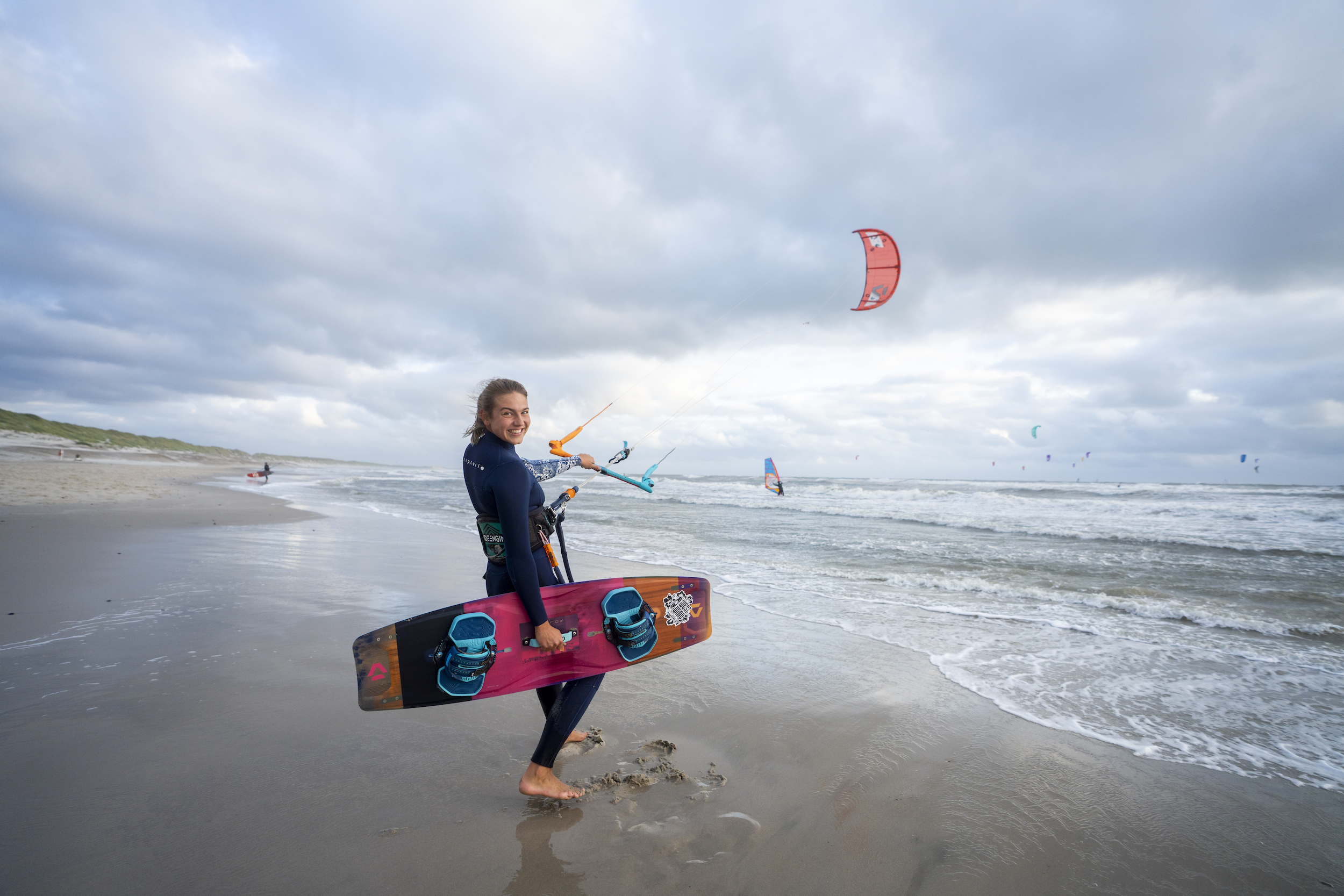 Pige står i strandkanten med kitesurf board