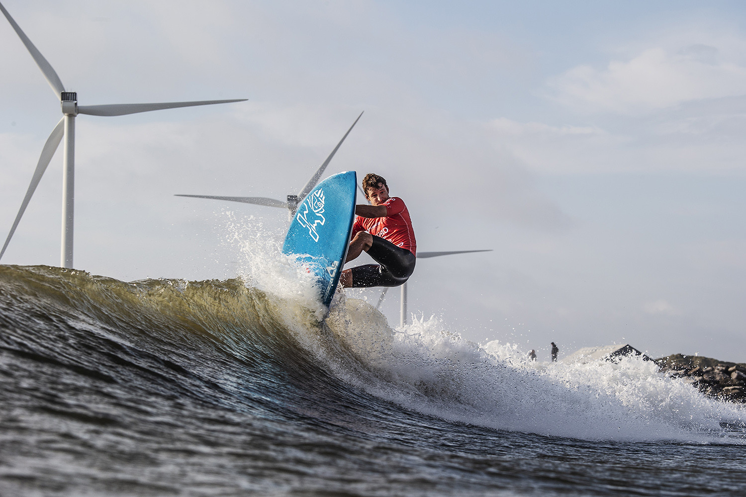 Surfer på en bølge med vindmøller i baggrunden