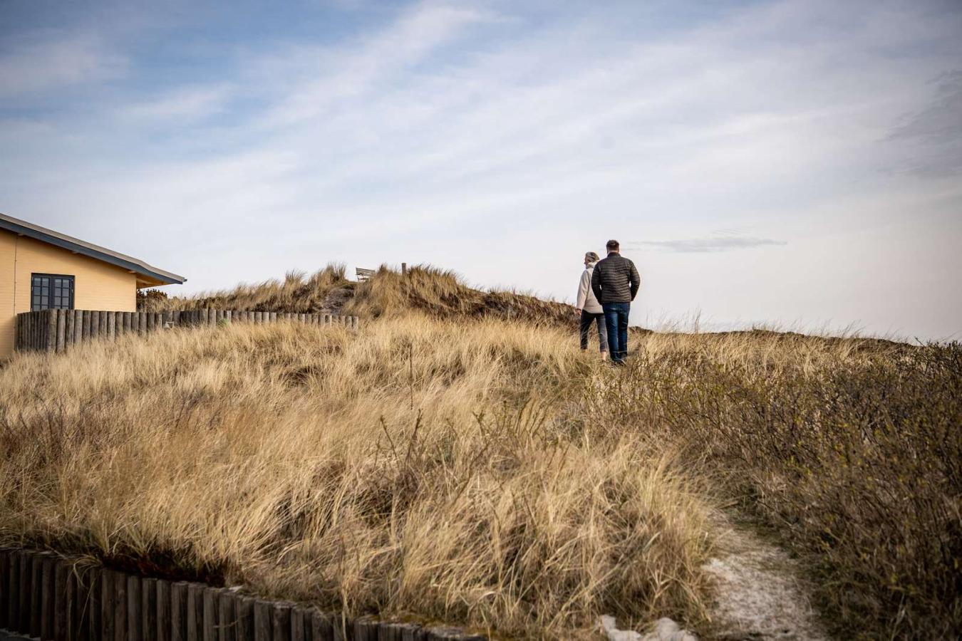 Et par går en tur ved et feriehus i klitlandskab