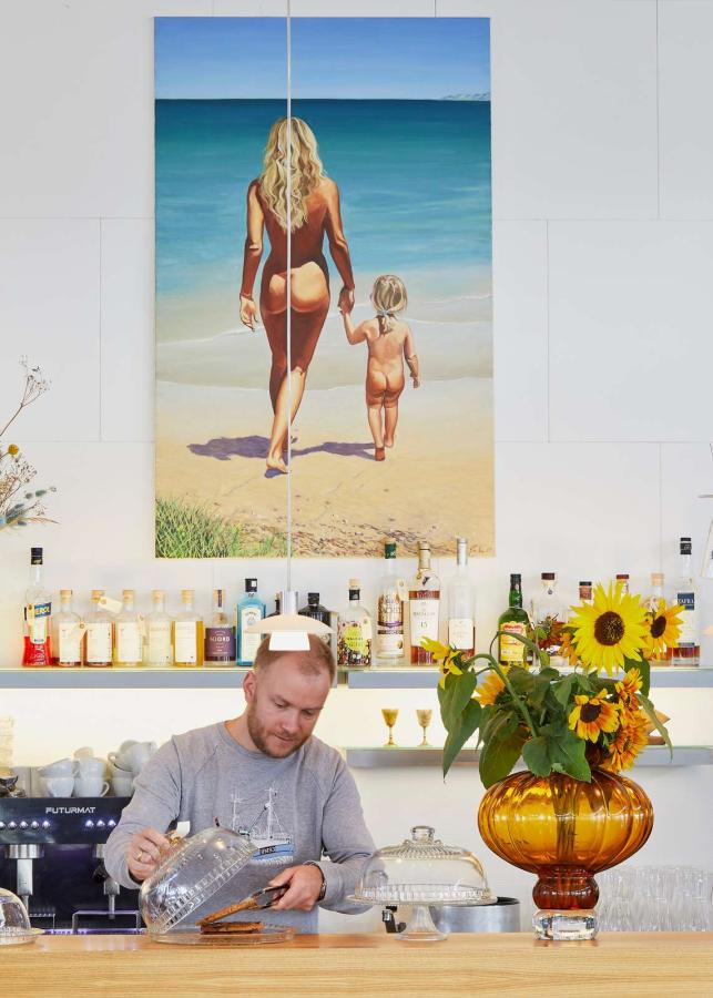 Mand i café med stort maleri af kvinde og barn på stranden