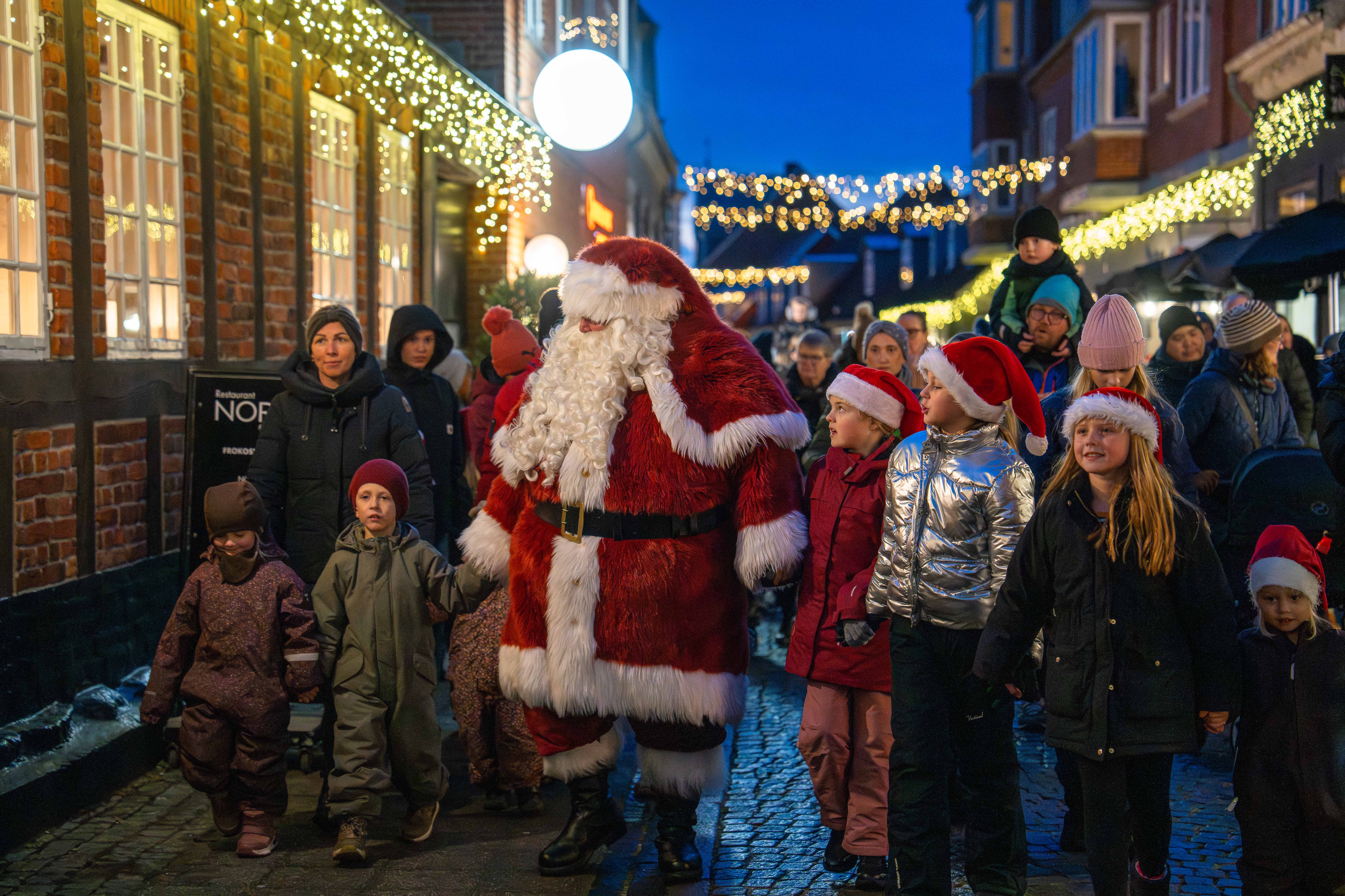 Julemanden går gennem en julepyntet gågade omgivet af børn og voksne