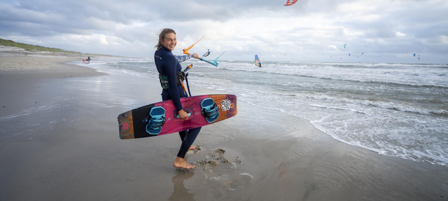 Pige står i strandkanten med kitesurf board