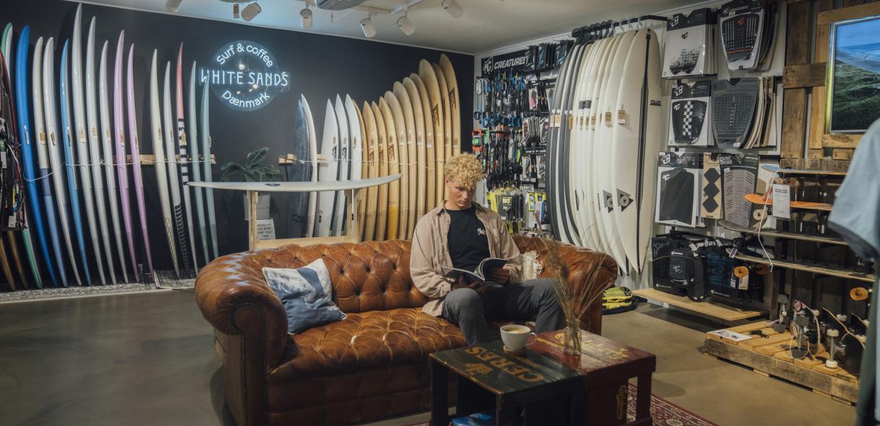 Mand sidder i surfbutik og læser magasin