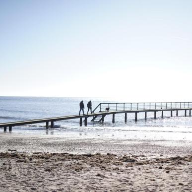 Par som går på stranden på vesterhavet ved en badebro