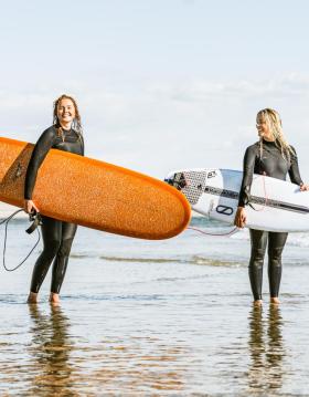 To damer som står i vandkanten med deres surfboards